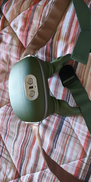 Le châle de massage Nuquea posé sur un couvre-lit rayé, ses boutons de commande visibles sur la coque verte