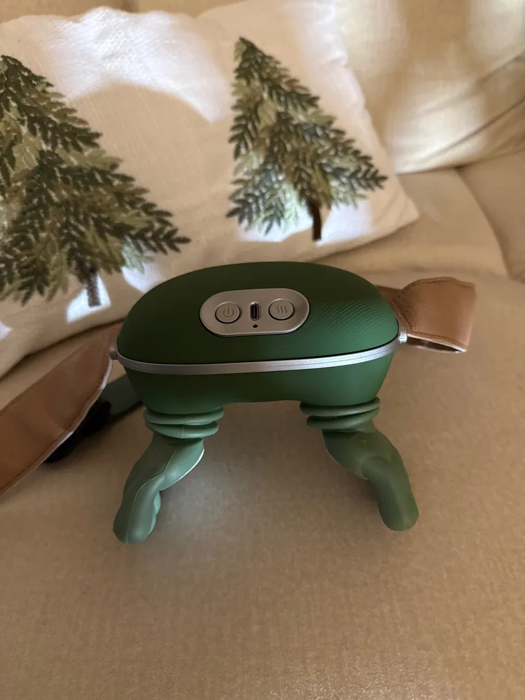 Le châle de massage Nuquea posé debout sur un canapé beige, ses boutons et son port de charge USB-C visibles