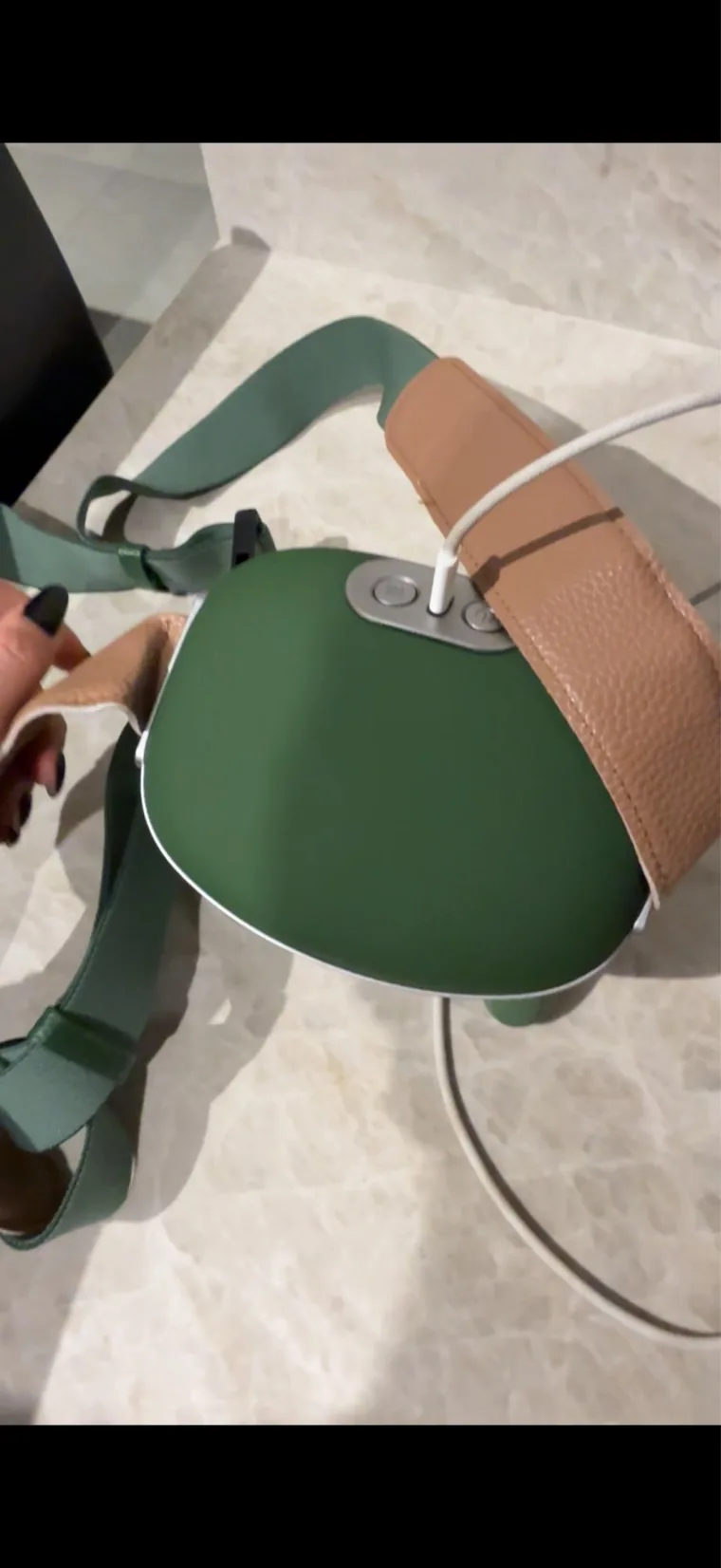 Le châle de massage Nuquea tenu à la main au-dessus d'un sol clair, câble de charge blanc branché